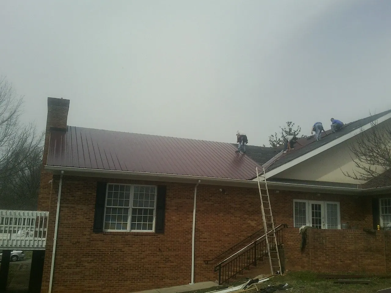Crew setting red metal roofing panels on a brick home in Torrance