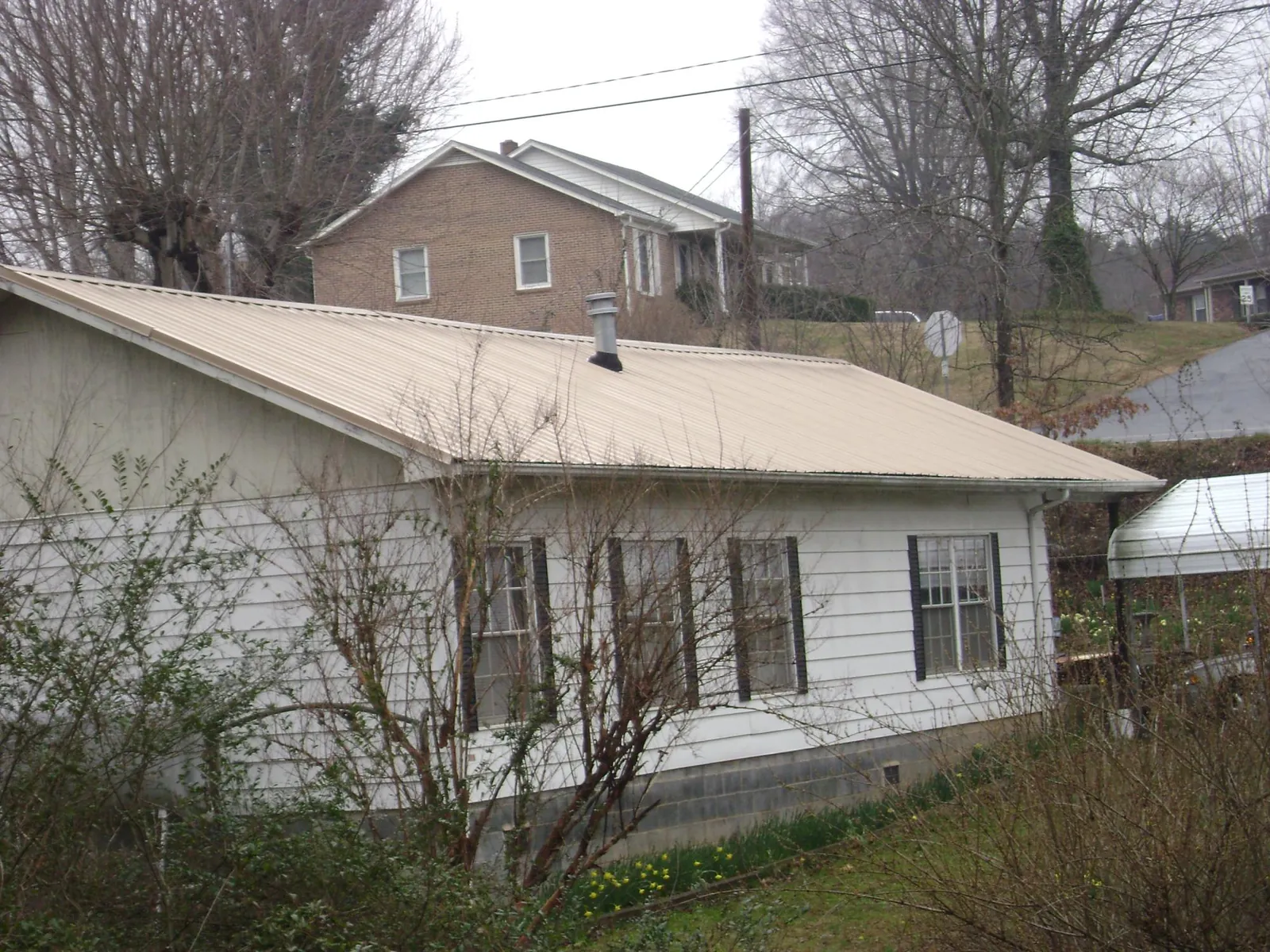 Tan metal roof on a white sided house set into a hillside — Commercial Roofing by Roofing Brothers in Torrance